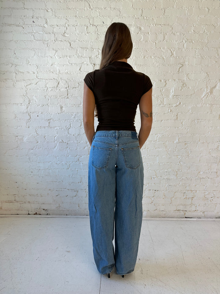 Woman wearing dark brown mock neck fitted top with medium wash jean and heel.