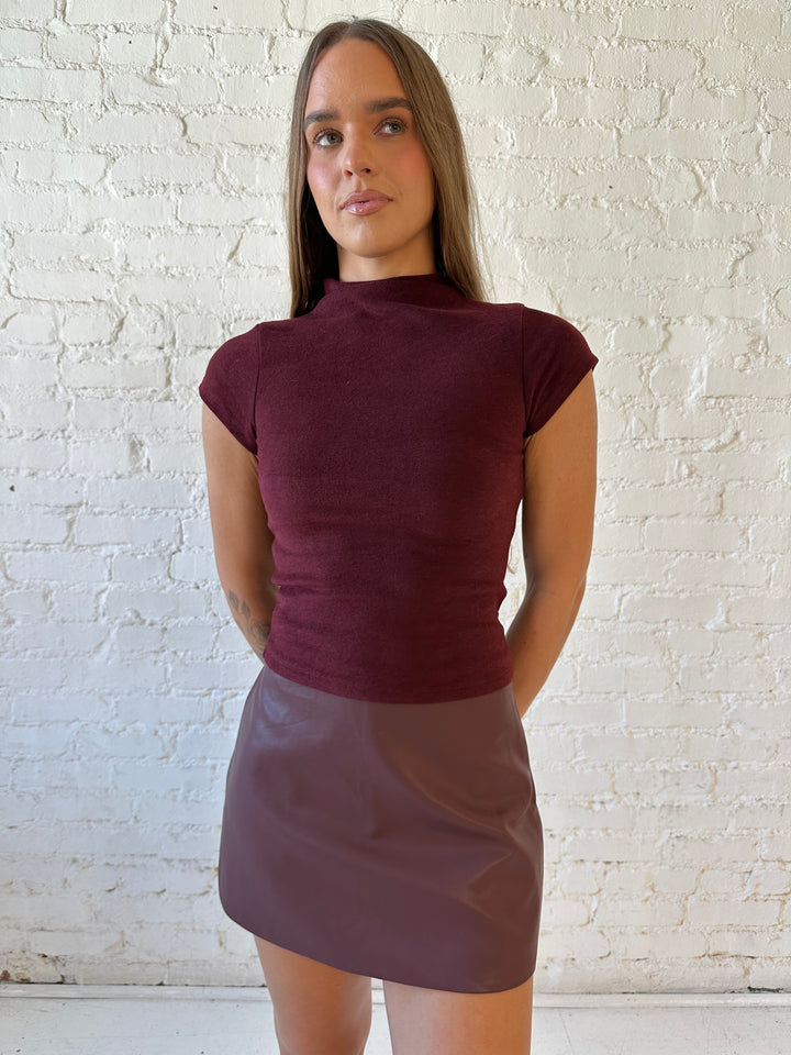 Woman wearing burgundy colored fitted mock neck top with burgundy mini skort.