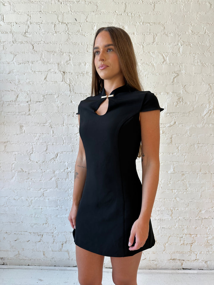 Woman wearing black mini dress with keyhole cutout and metal detail along the neckline. 