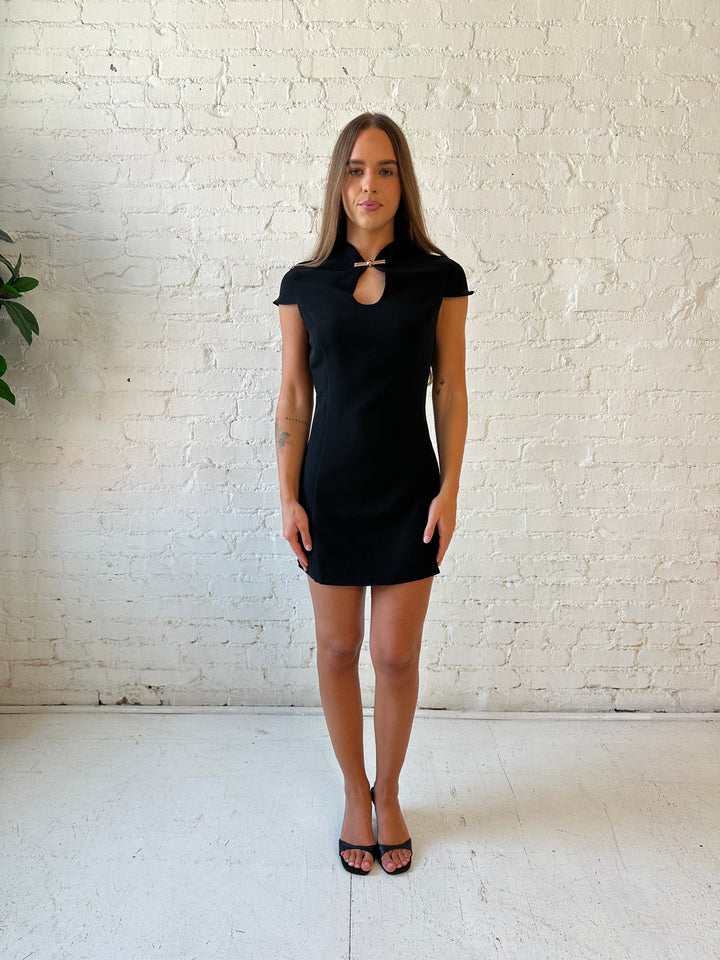 Woman wearing black mini dress with keyhole cutout and metal detail along the neckline. 