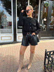Woman wearing black knit button down cardigan and black leather short. 