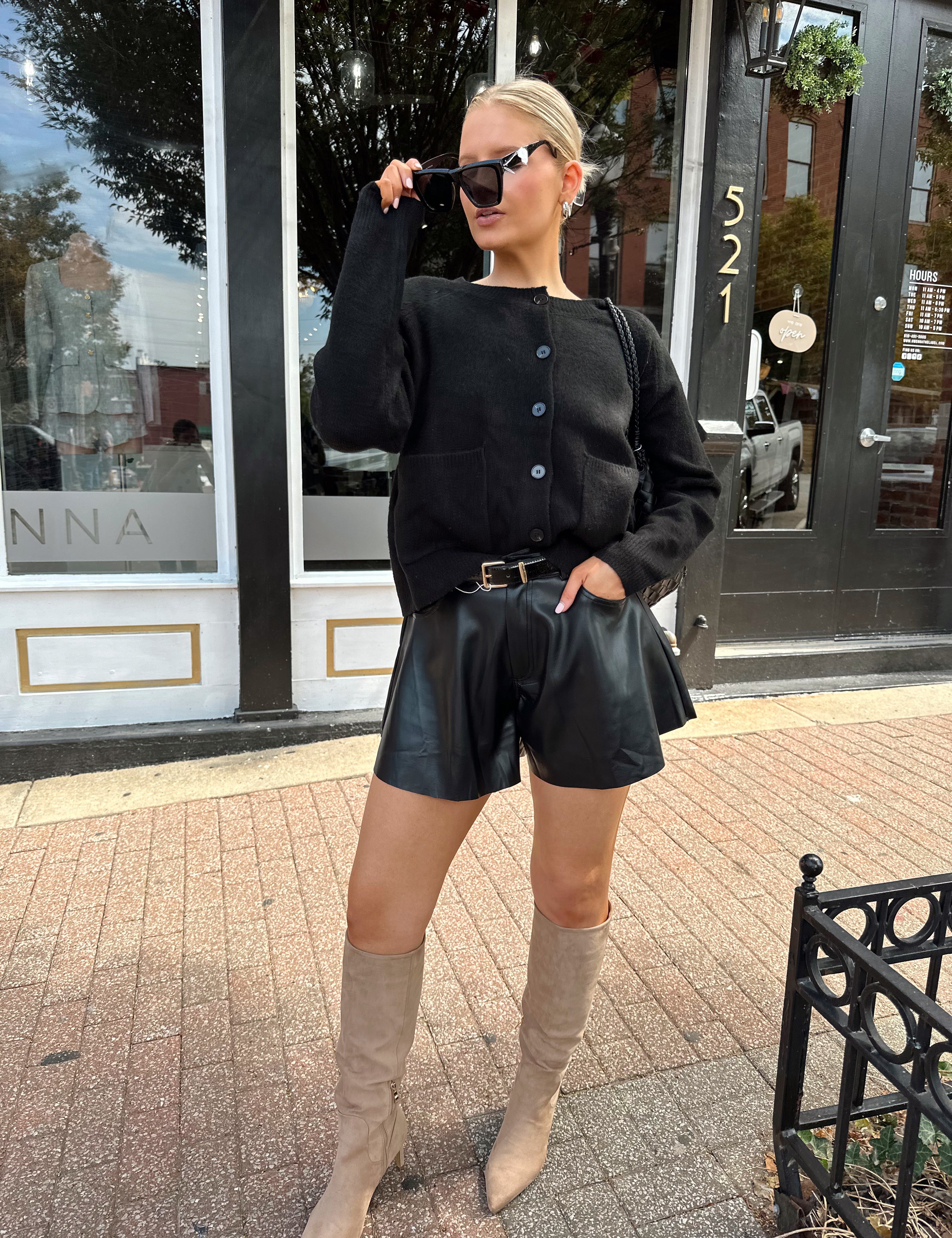 Woman wearing black knit button down cardigan and black leather short. 