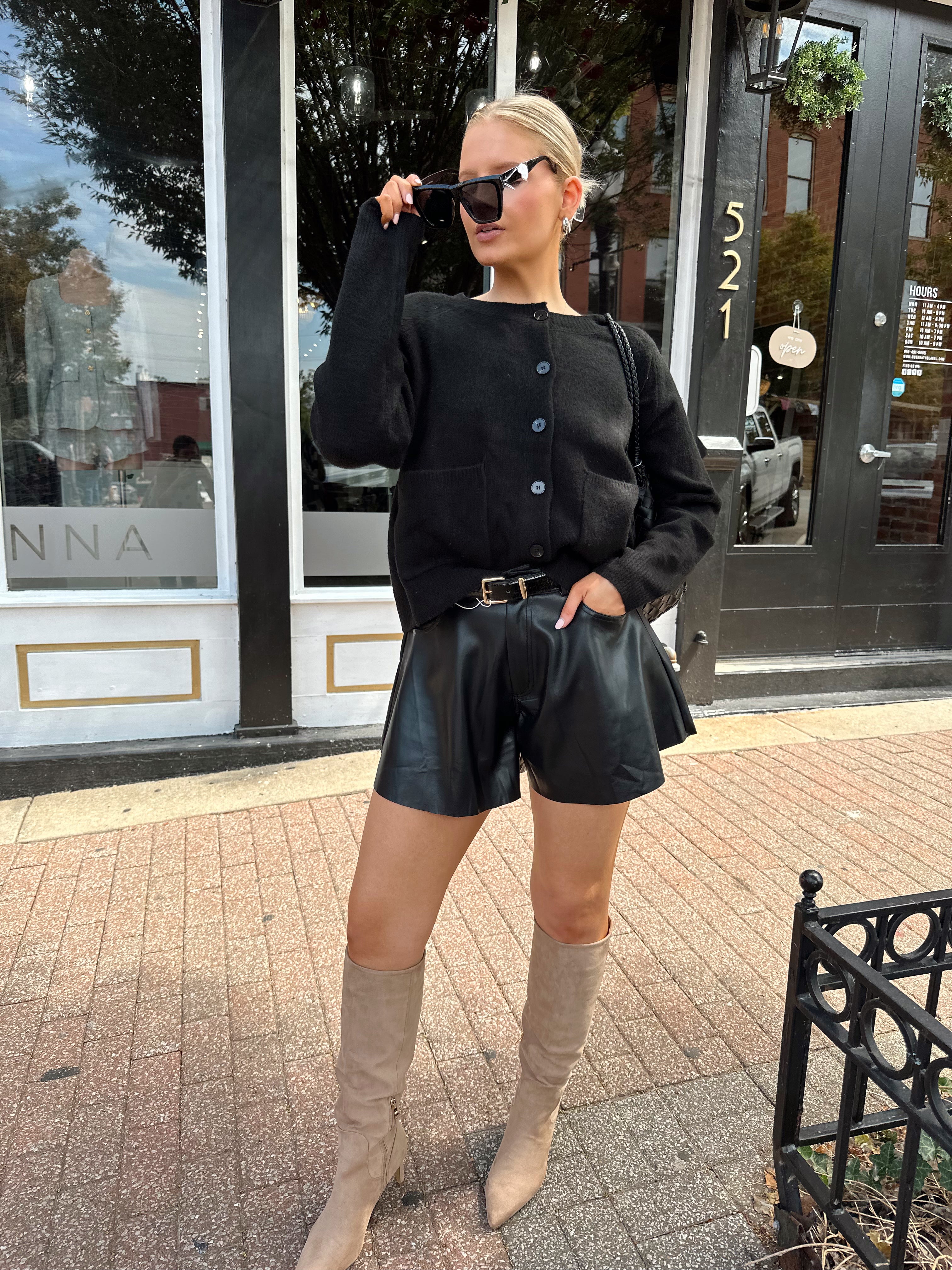 Woman wearing black knit button down cardigan and black leather short. 