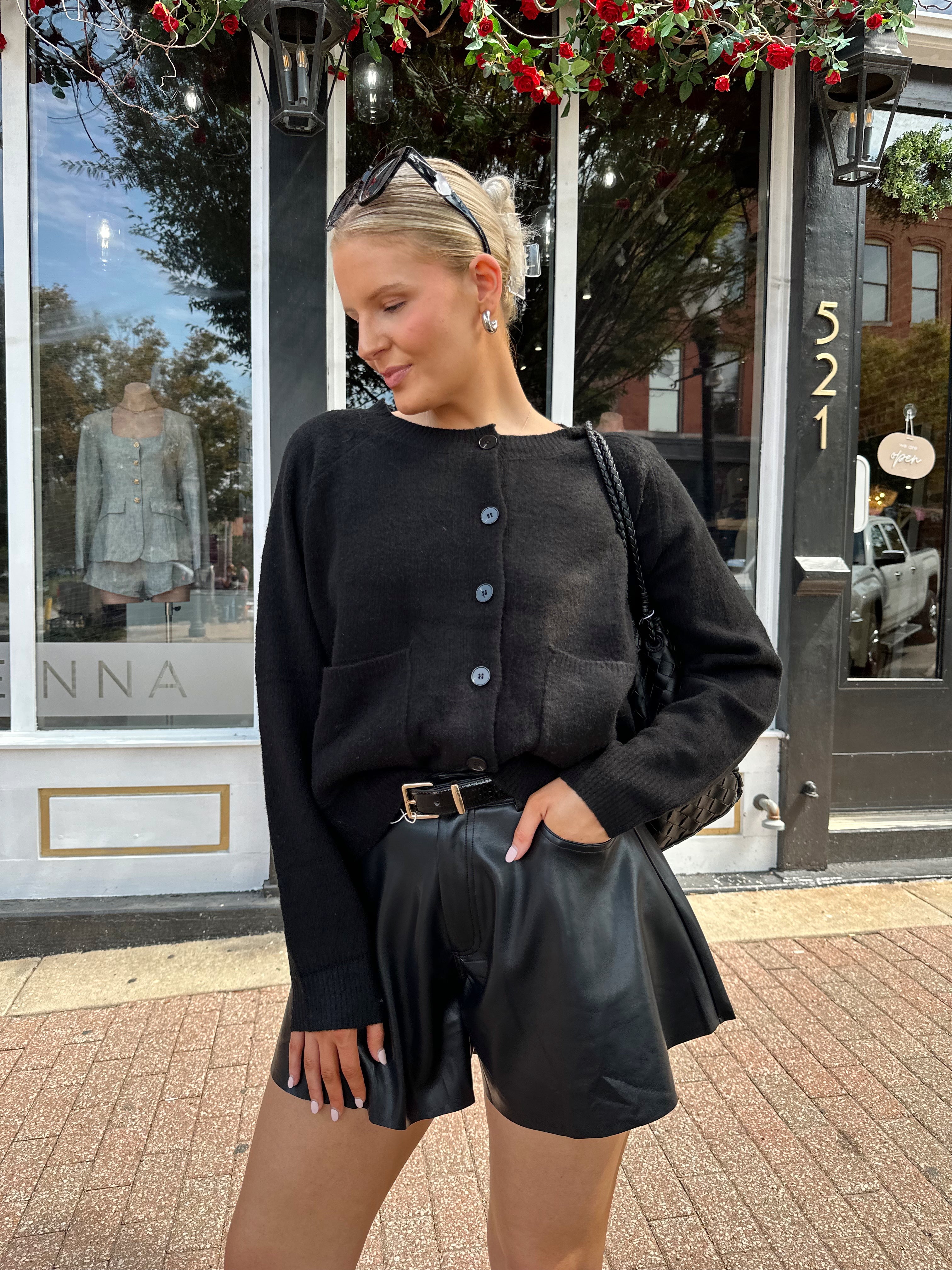 Woman wearing black knit button down cardigan and black leather short. 