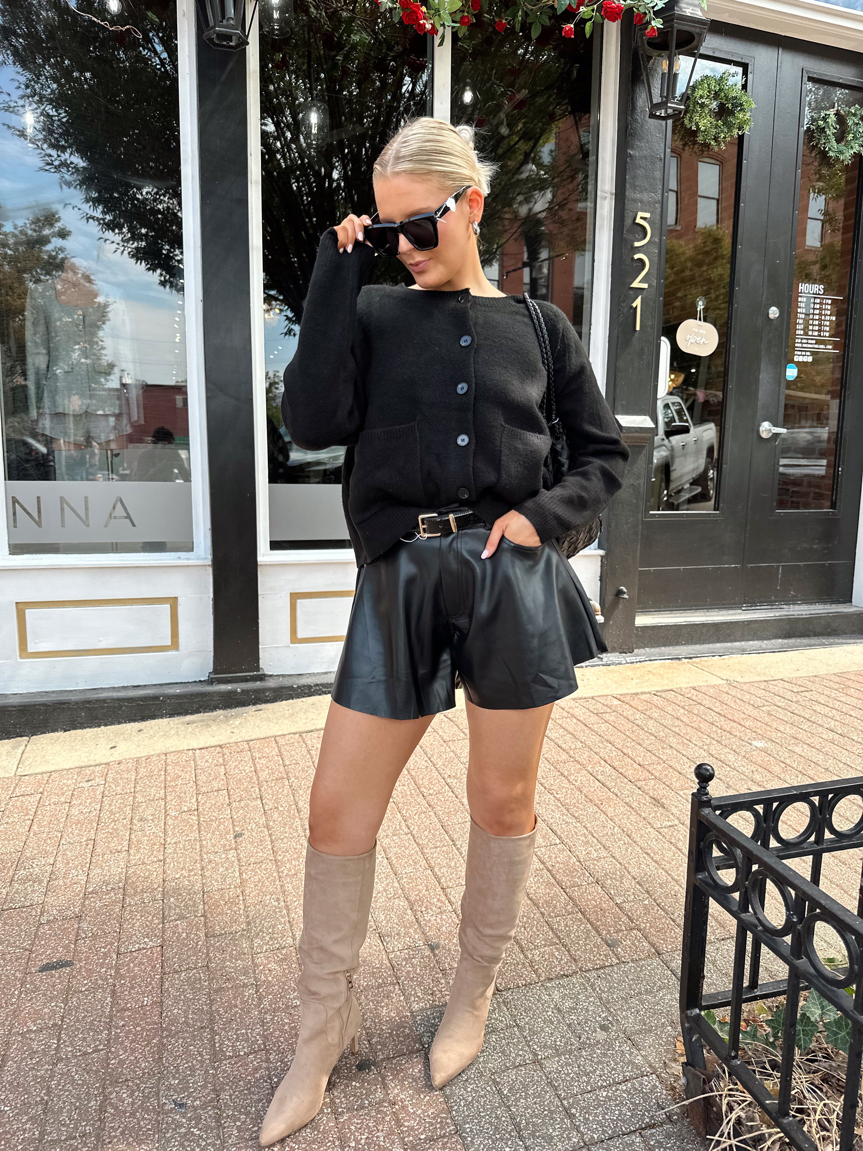 Woman wearing black knit button down cardigan and black leather short. 