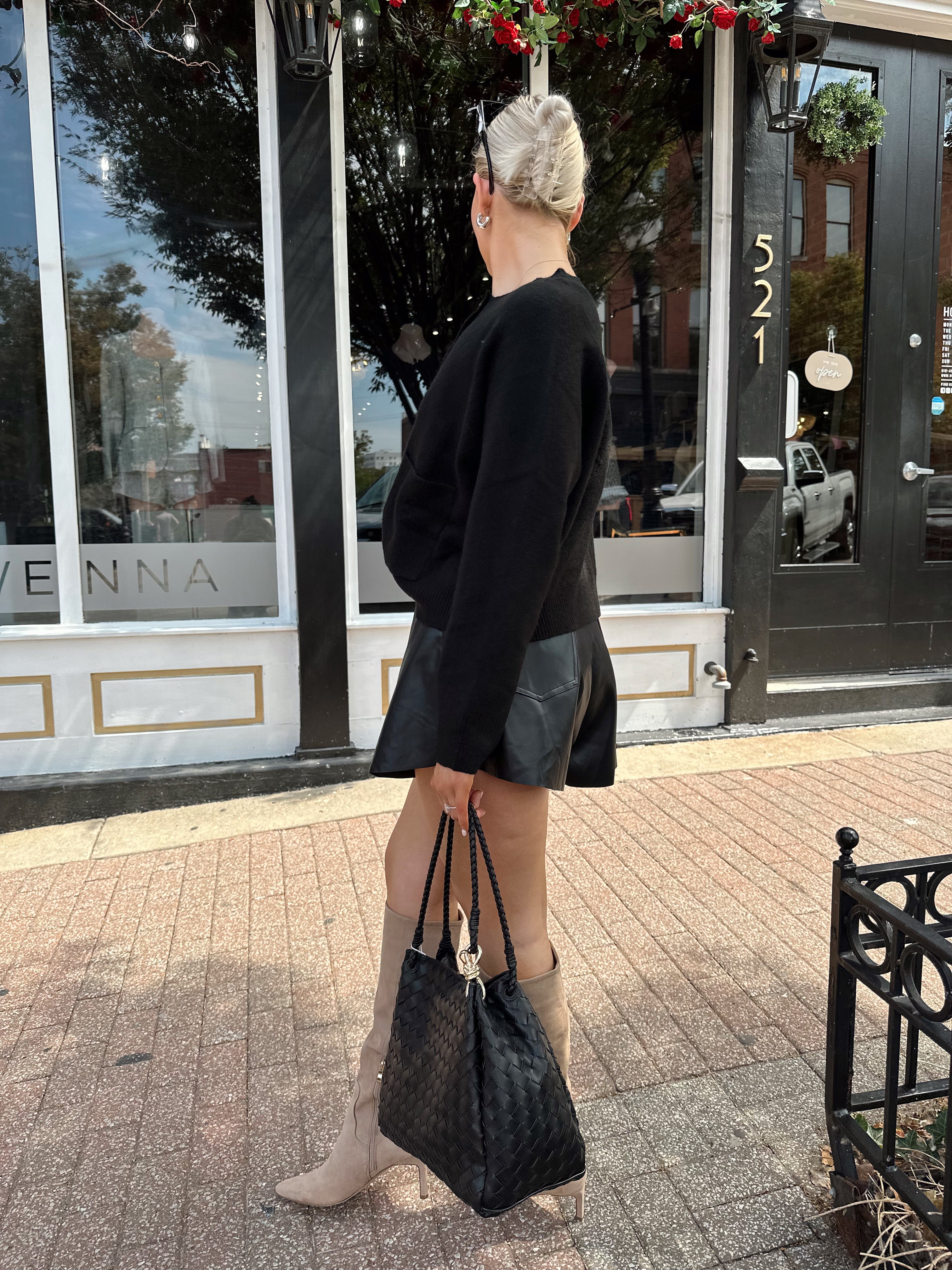 Woman wearing black knit button down cardigan and black leather short. 