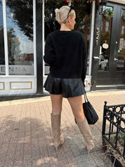 Woman wearing black knit button down cardigan and black leather short. 