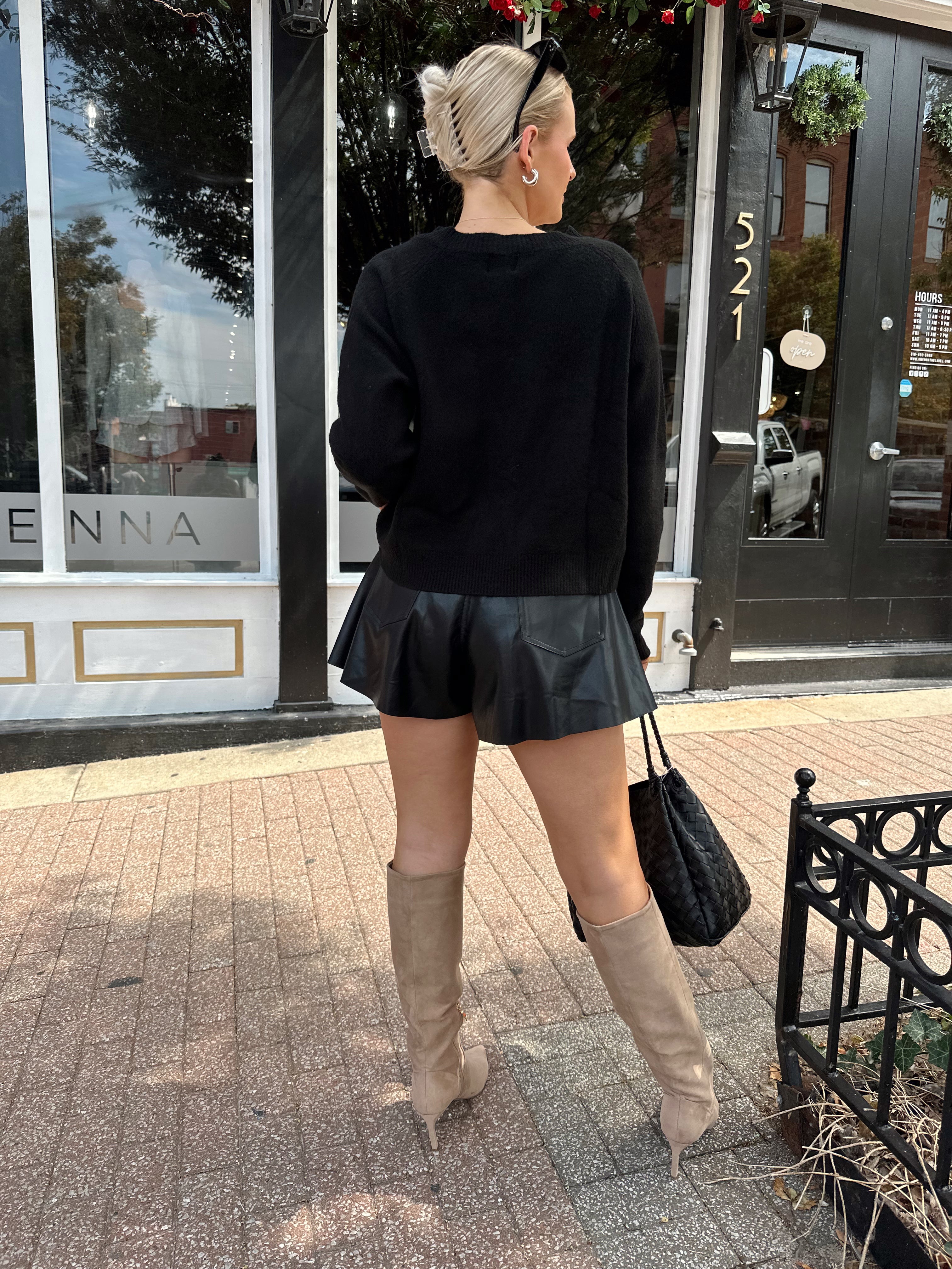 Woman wearing black knit button down cardigan and black leather short. 