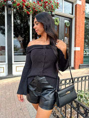 Woman wearing ribbed long sleeve off the shoulder black top with button detail.