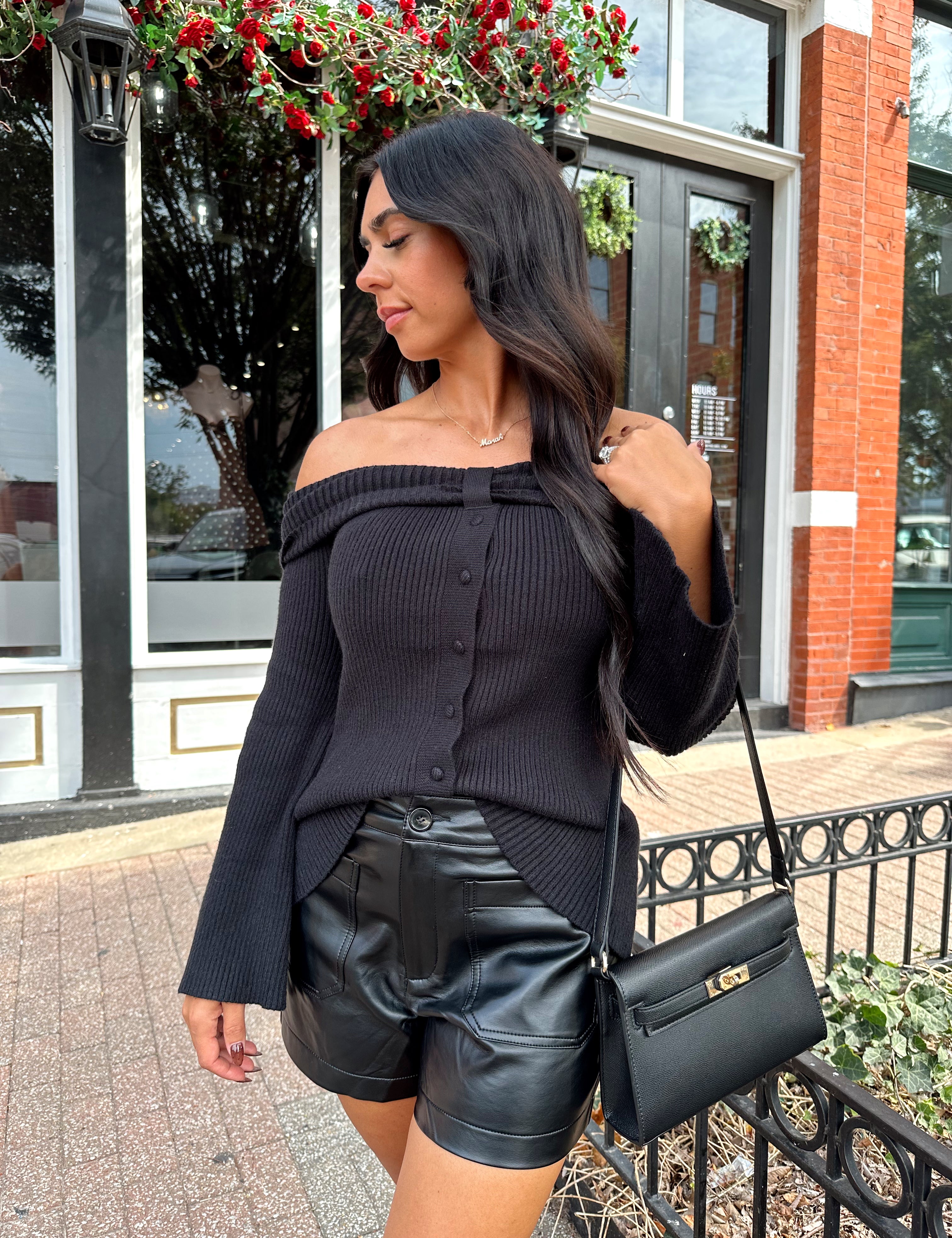 Woman wearing ribbed long sleeve off the shoulder black top with button detail.