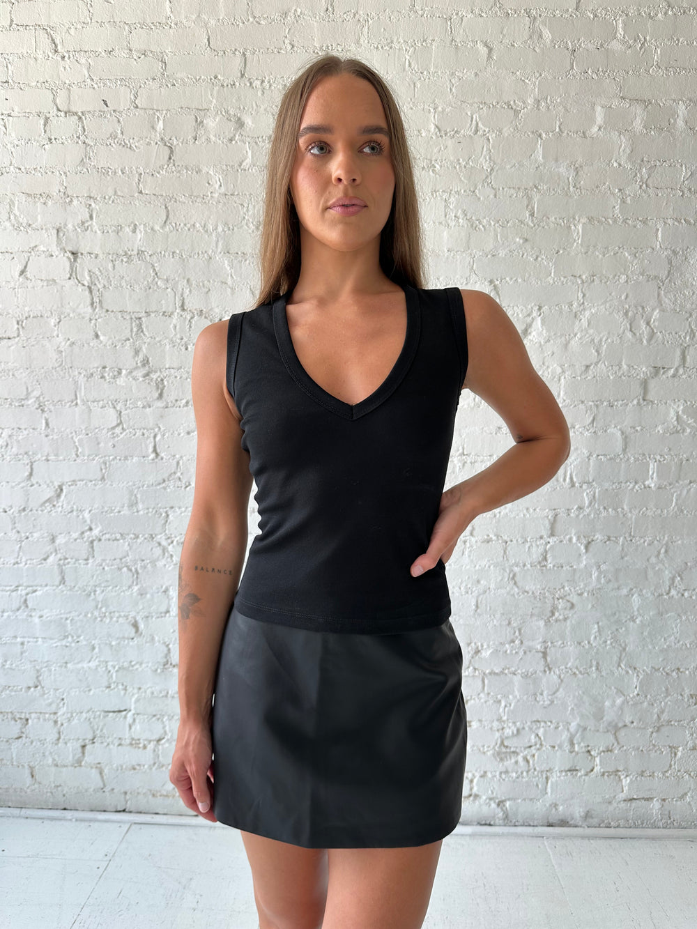 Woman wearing black fitted tank top with v-neckline, and a black leather mini skort. 