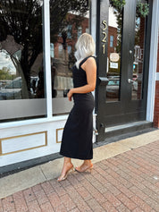 Woman wearing a black square neck fitted midi dress with clear heels outside a storefront.
