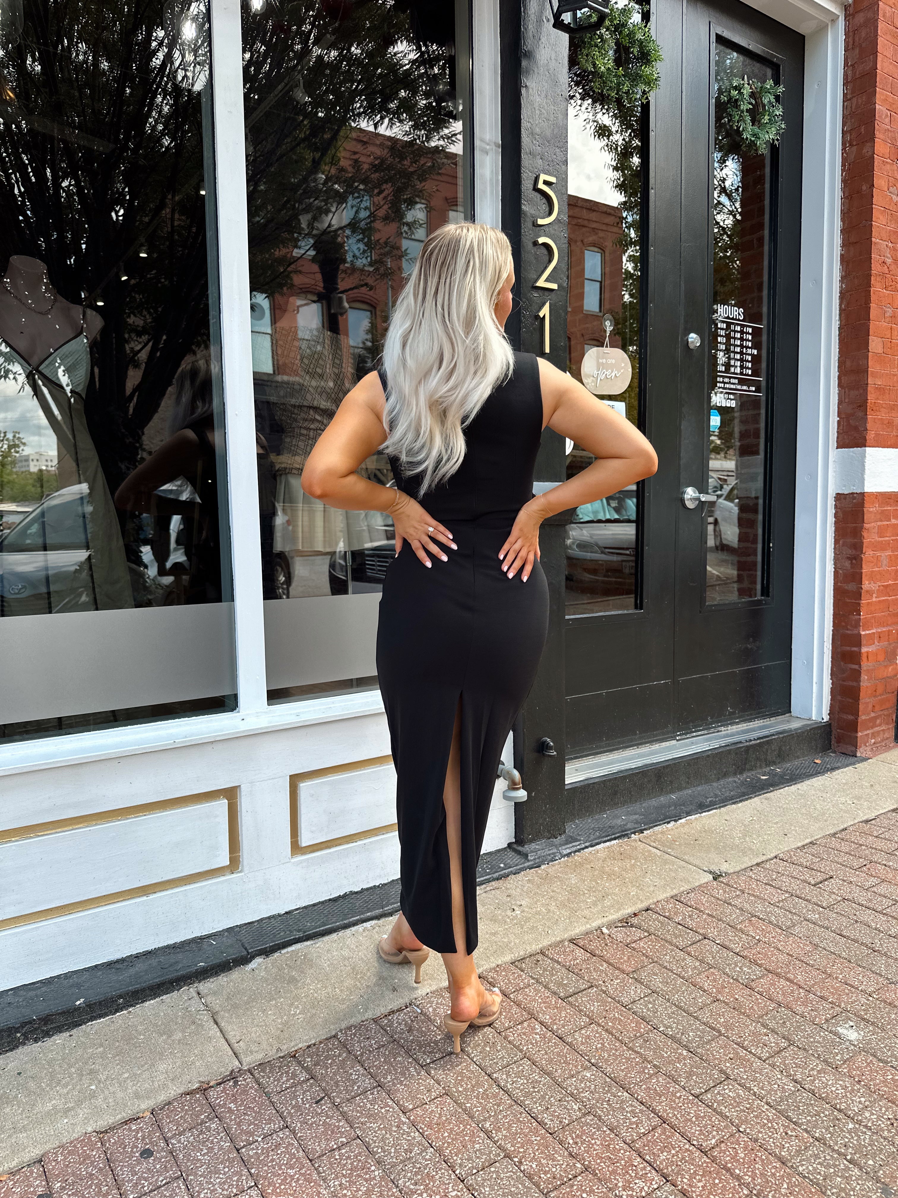 Woman wearing a black square neck fitted midi dress with clear heels outside a storefront.