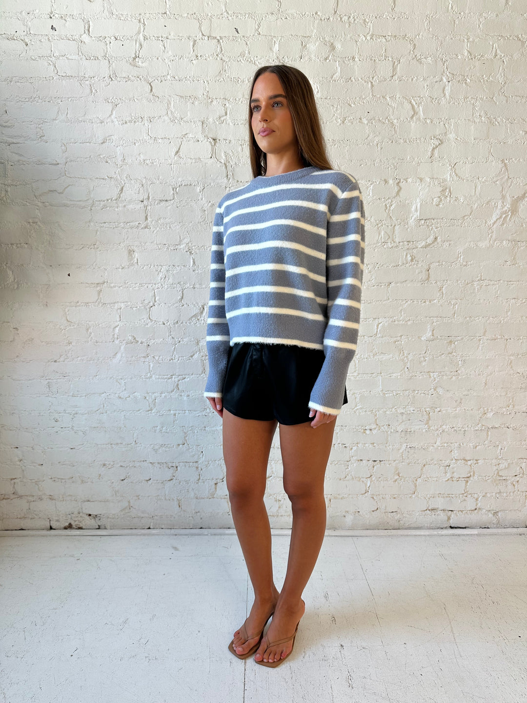 Woman wearing blue and white striped crew neck sweater and high waisted black faux leather shorts. 