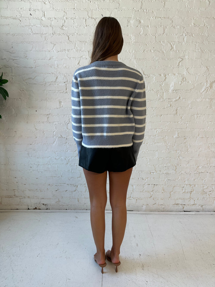 Woman wearing blue and white striped crew neck sweater and high waisted black faux leather shorts. 