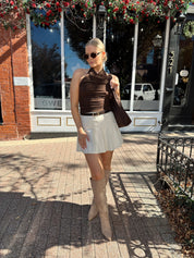 Woman wearing brown mesh, cowl, halter neck top.