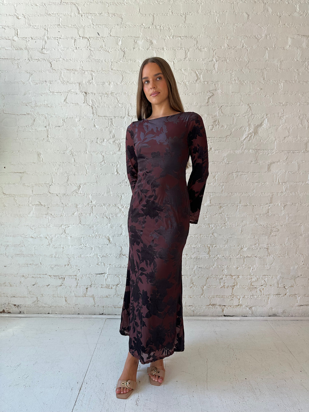 Woman wearing long sleeve burgundy, floral velvet, long sleeve maxi dress with open cutout back. 