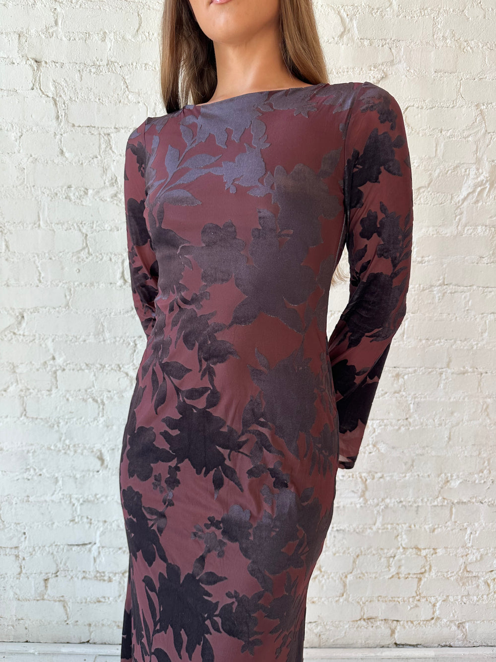 Woman wearing long sleeve burgundy, floral velvet, long sleeve maxi dress with open cutout back. 