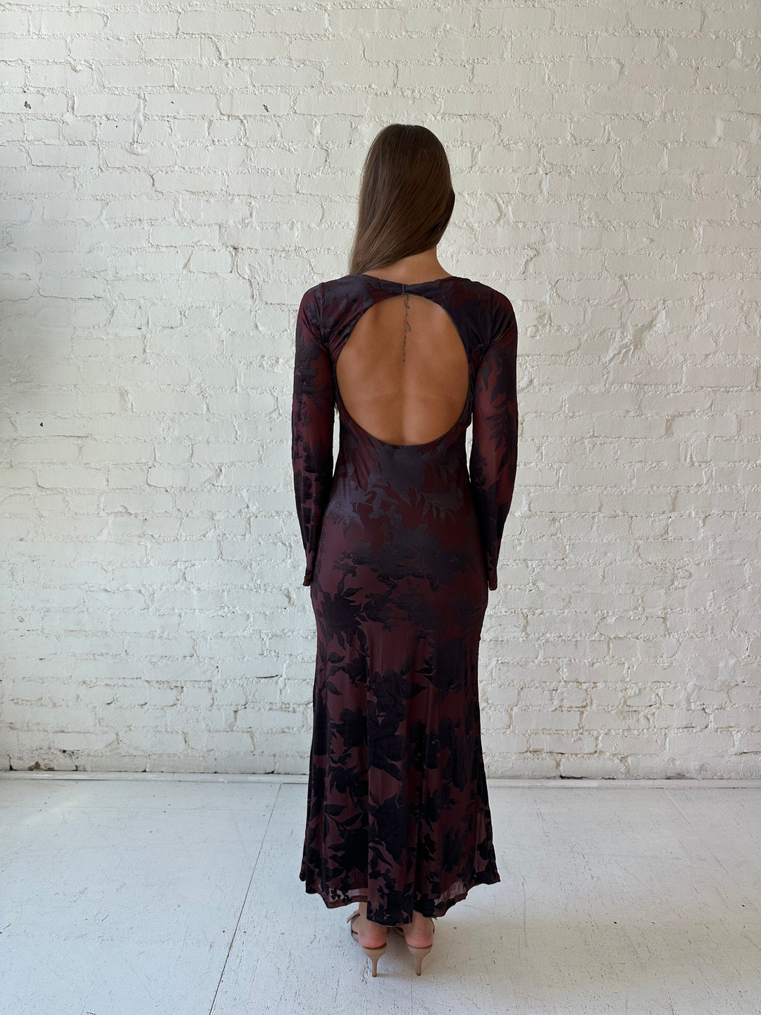 Woman wearing long sleeve burgundy, floral velvet, long sleeve maxi dress with open cutout back. 