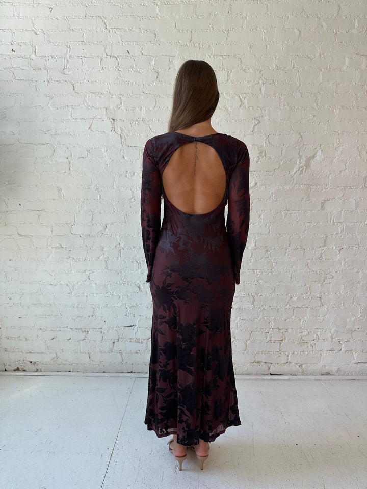 Woman wearing long sleeve burgundy, floral velvet, long sleeve maxi dress with open cutout back. 