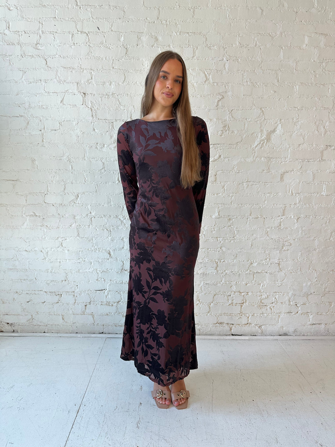 Woman wearing long sleeve burgundy, floral velvet, long sleeve maxi dress with open cutout back. 