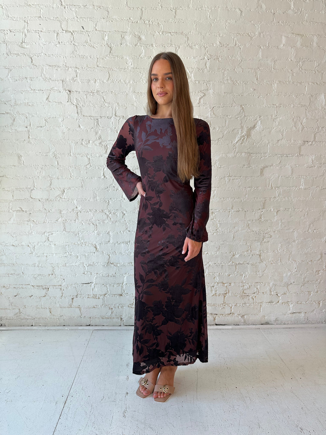 Woman wearing long sleeve burgundy, floral velvet, long sleeve maxi dress with open cutout back. 