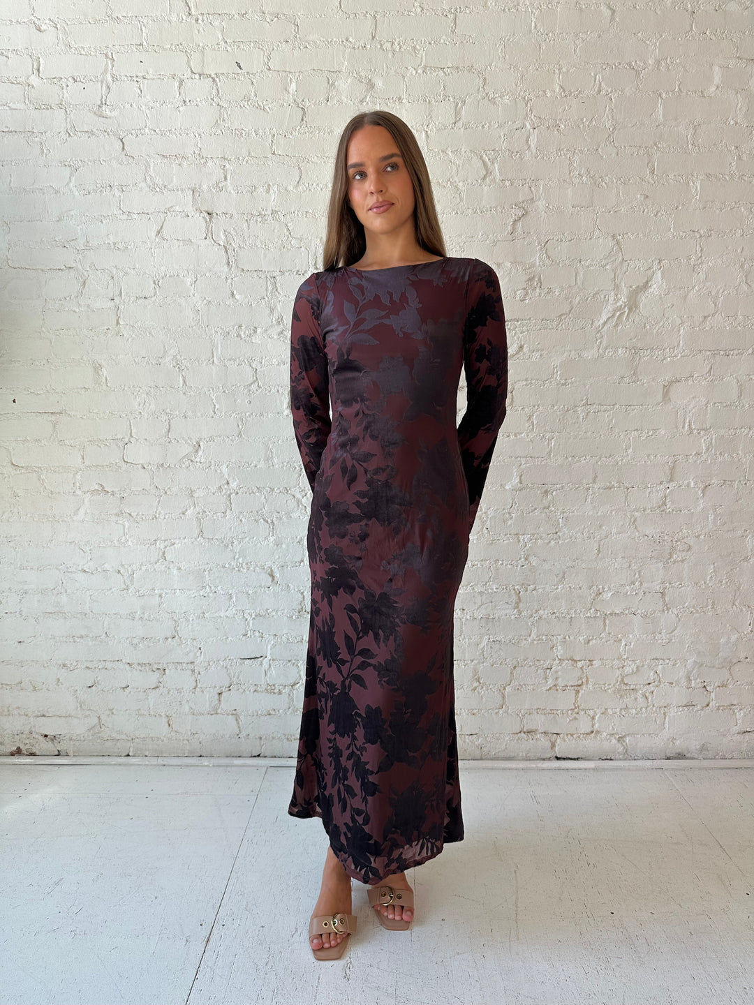 Woman wearing long sleeve burgundy, floral velvet, long sleeve maxi dress with open cutout back. 