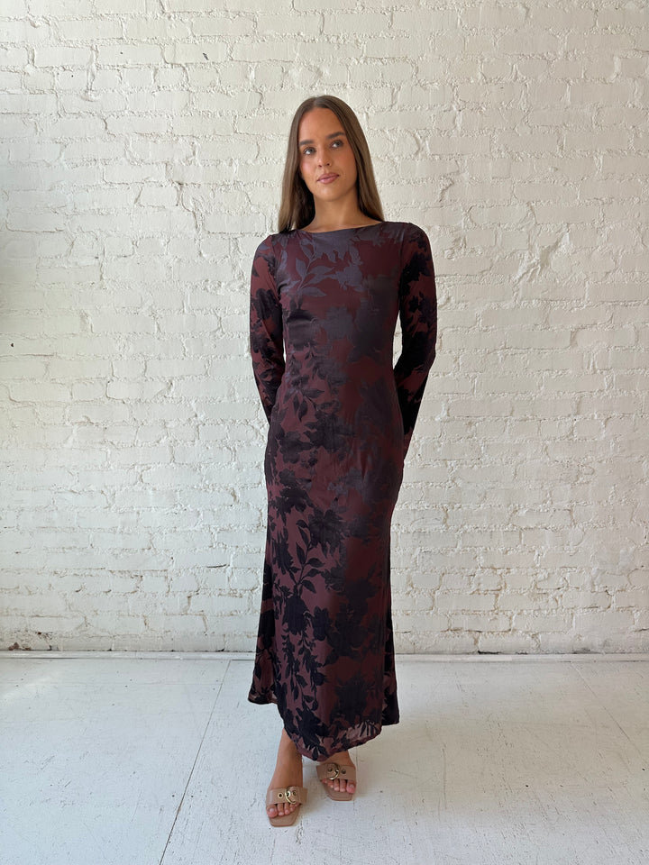 Woman wearing long sleeve burgundy, floral velvet, long sleeve maxi dress with open cutout back. 