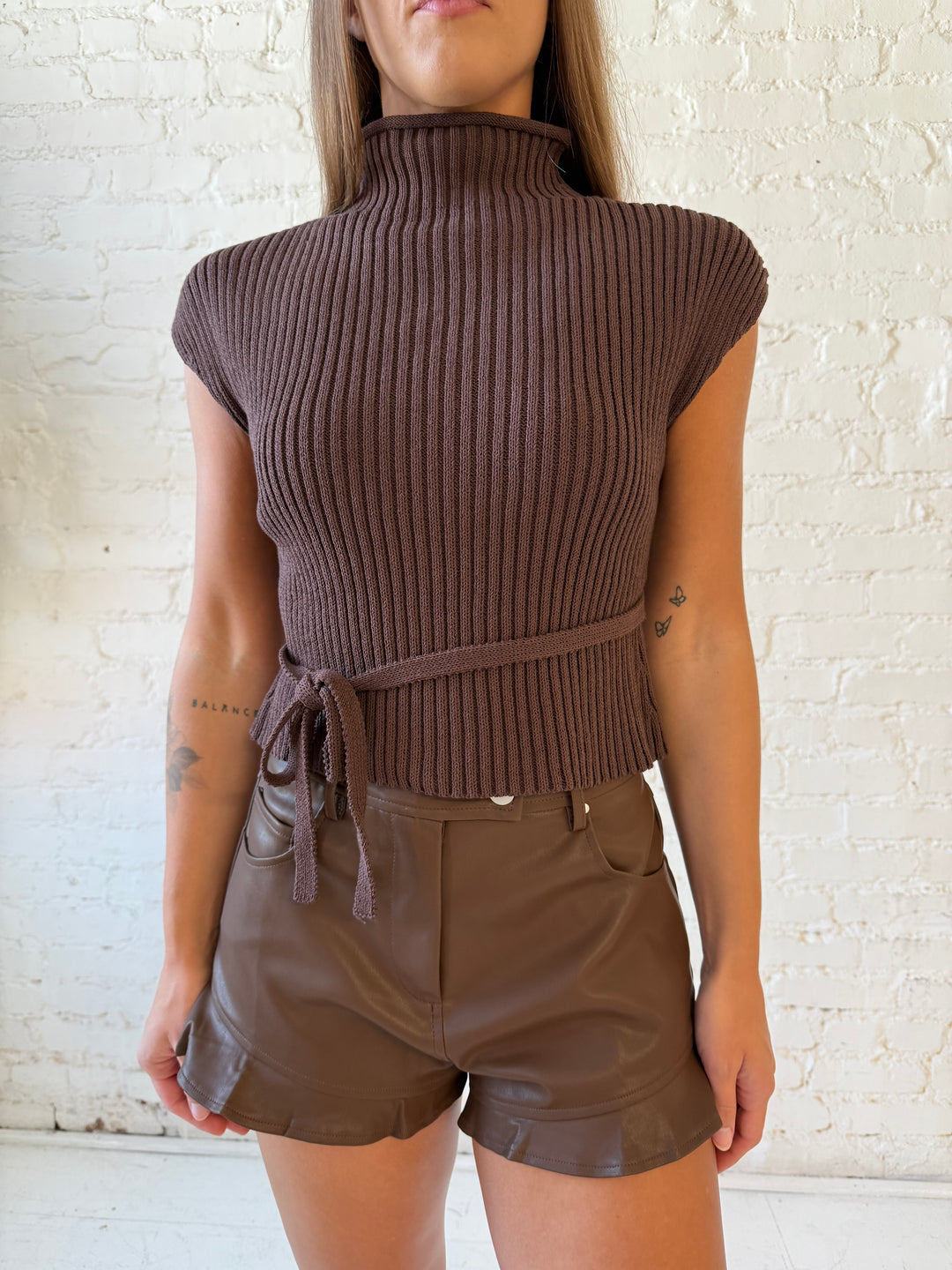 Woman wearing brown faux leather high waisted leather shorts with ruffle trim. 