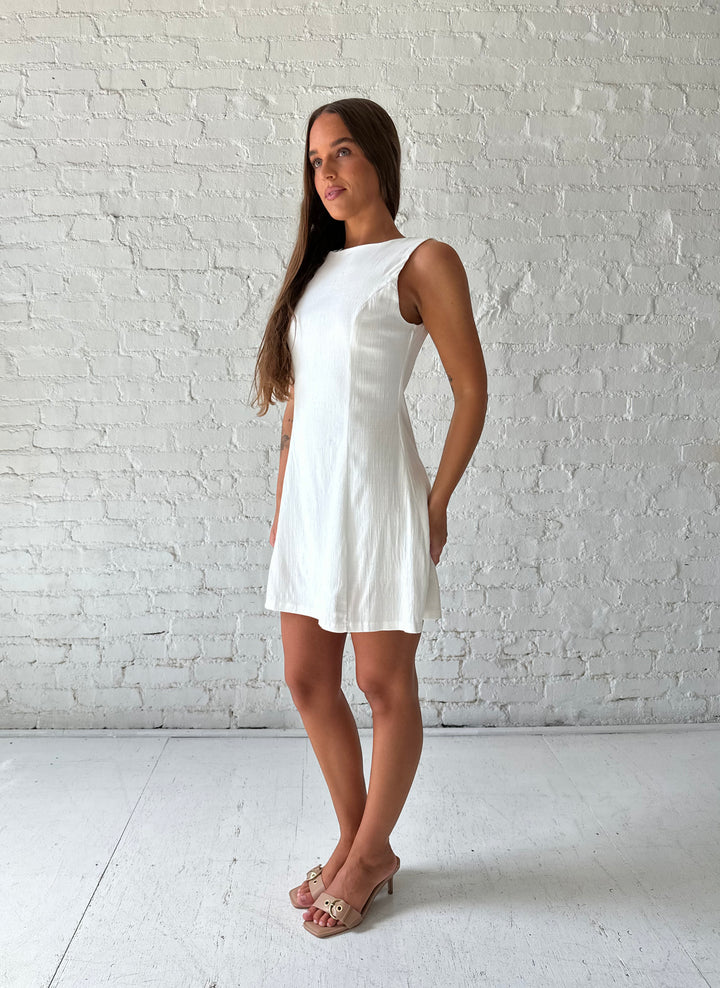 Woman wearing white stretch linen a-line mini dress with scoop back. 