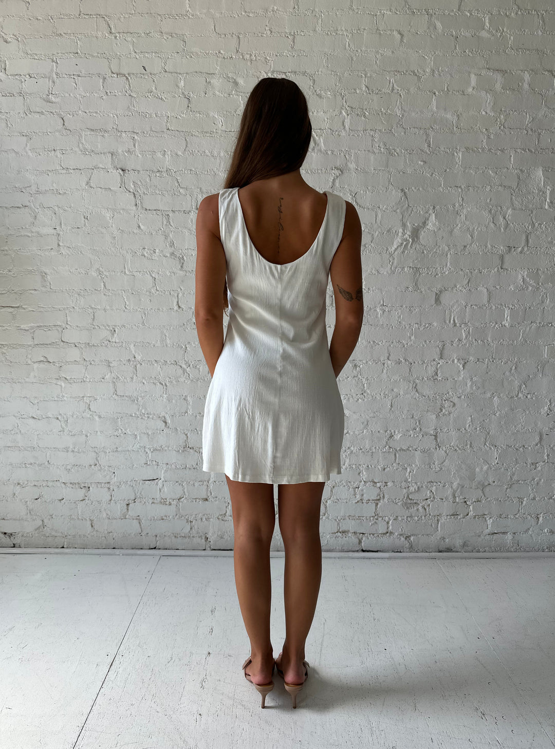Woman wearing white stretch linen a-line mini dress with scoop back. 