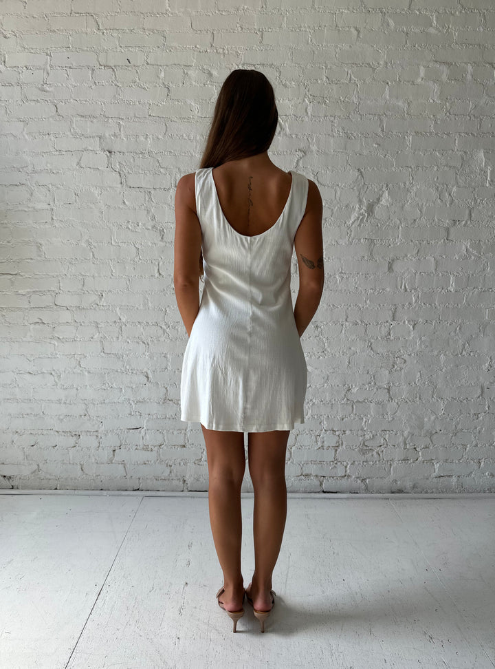 Woman wearing white stretch linen a-line mini dress with scoop back. 
