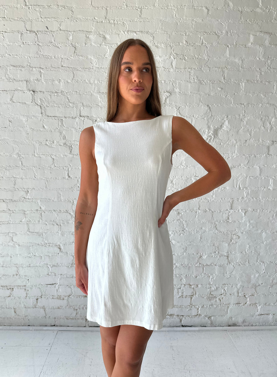 Woman wearing white stretch linen a-line mini dress with scoop back. 