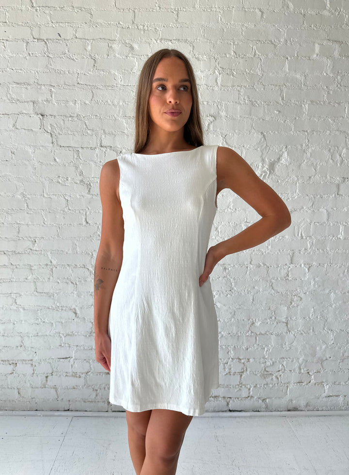 Woman wearing white stretch linen a-line mini dress with scoop back. 
