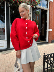 Red oversized button down cardigan with cream leather pleated mini skirt. 