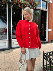 Red oversized button down cardigan with cream leather pleated mini skirt. 