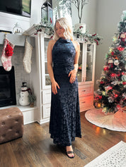 Woman wearing navy blue floral velvet maxi dress with halter neckline. 