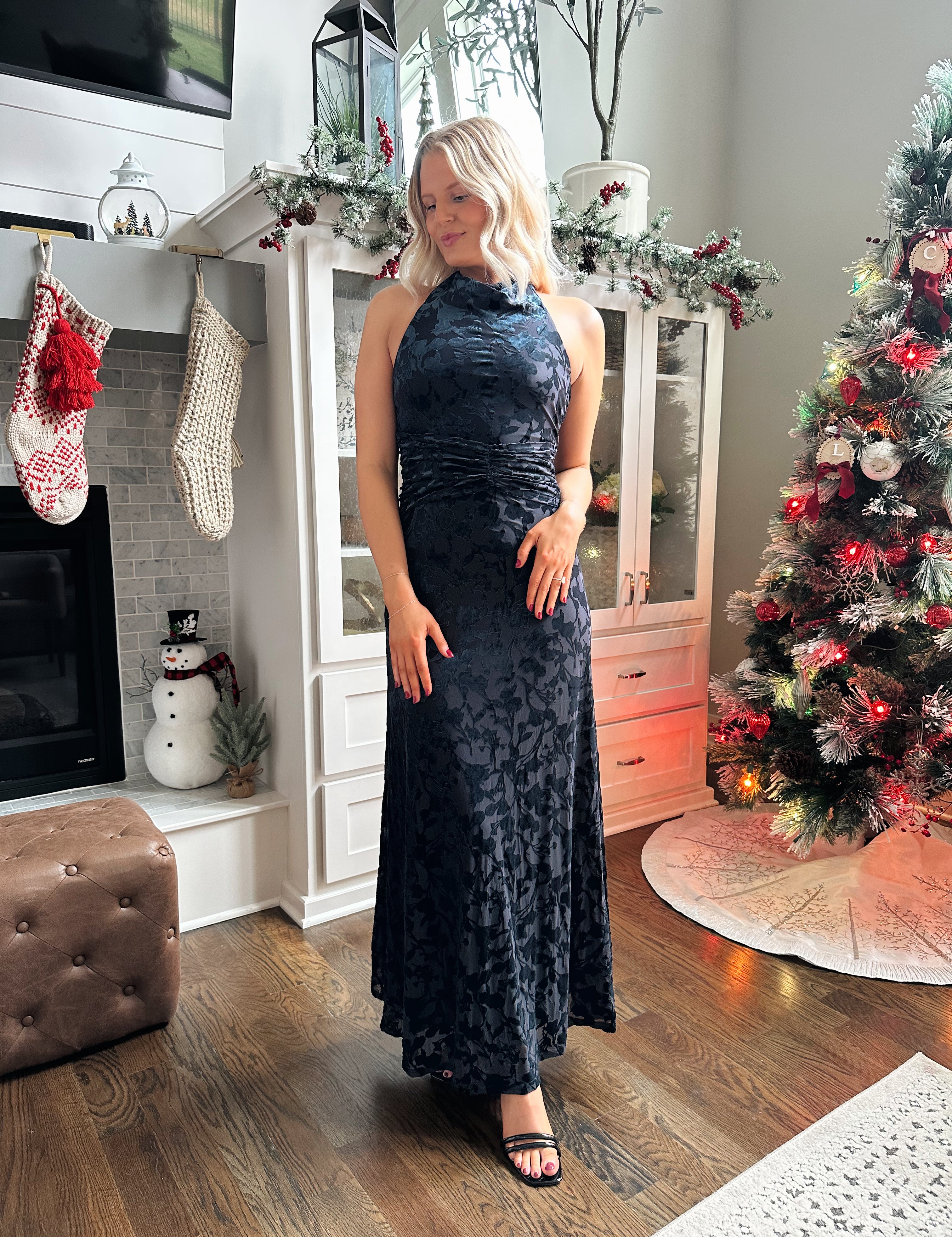 Woman wearing navy blue floral velvet maxi dress with halter neckline. 