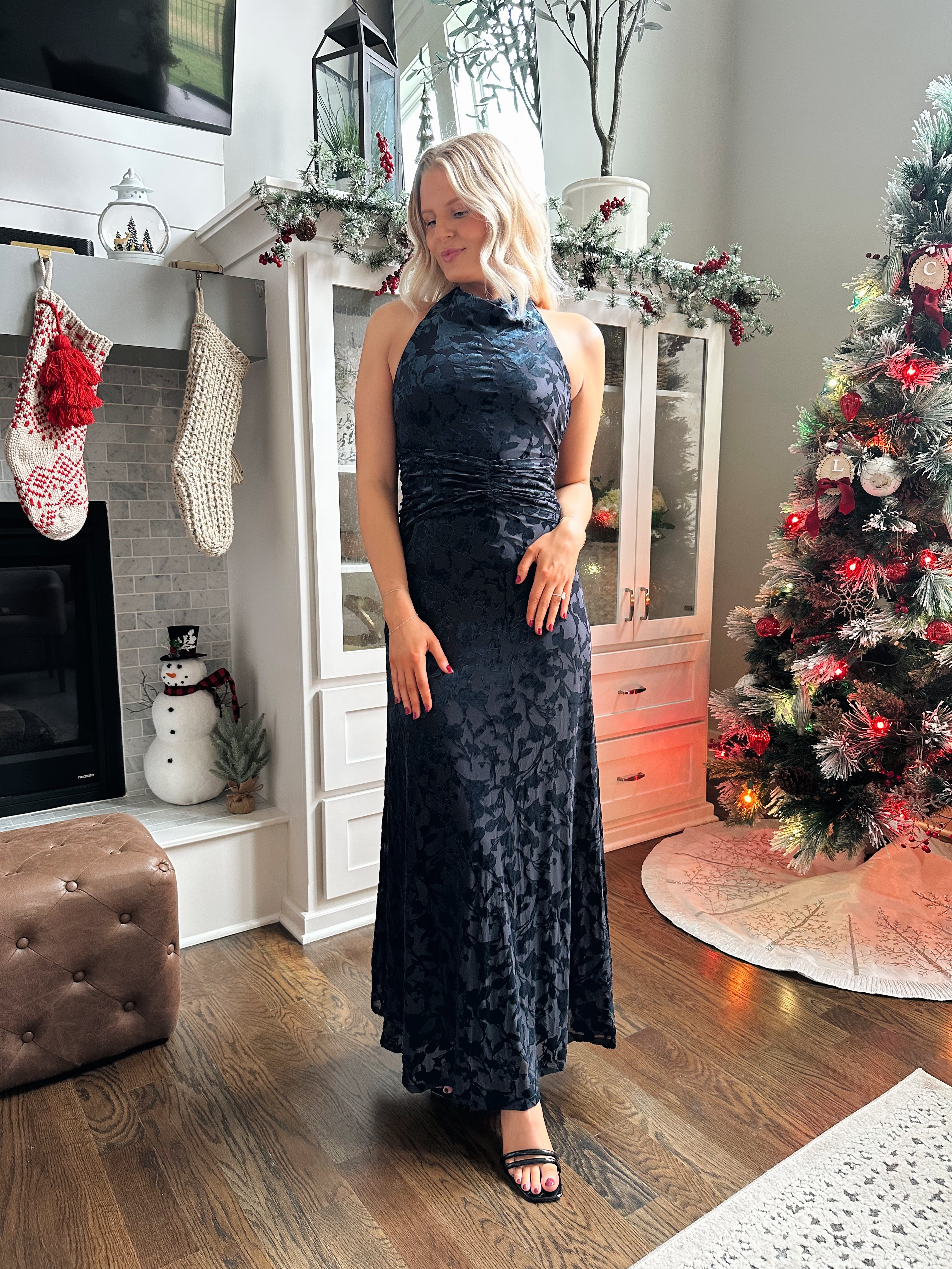 Woman wearing navy blue floral velvet maxi dress with halter neckline. 