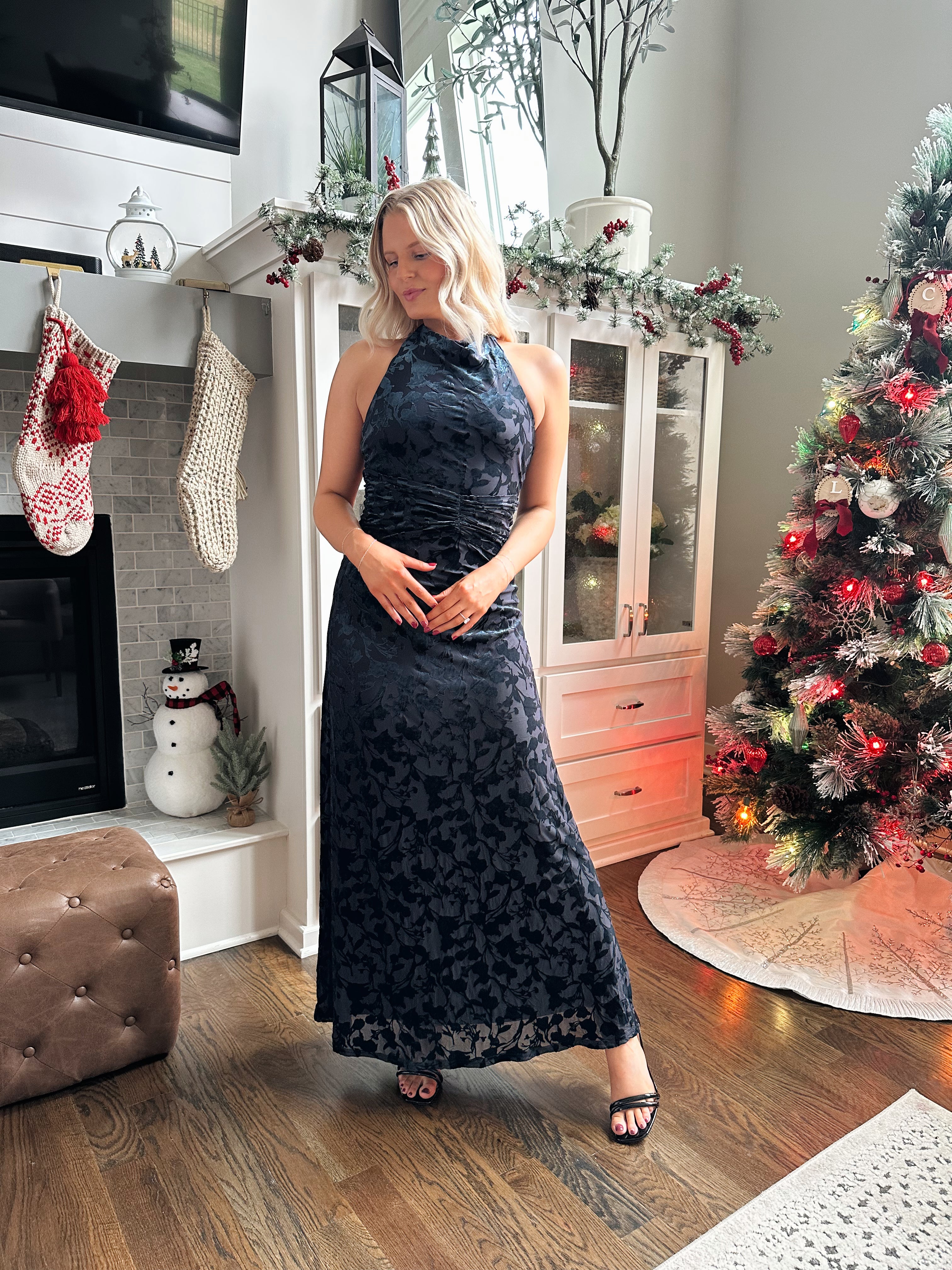 Woman wearing navy blue floral velvet maxi dress with halter neckline. 