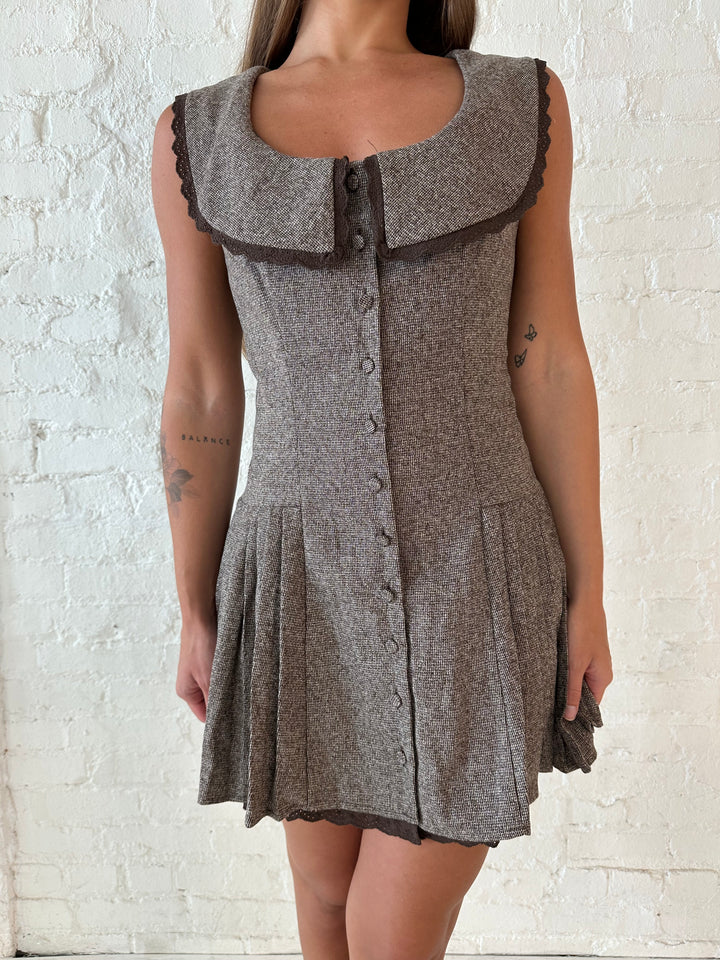 Woman wearing brown textured mini dress with collar detail, and pleated sides.