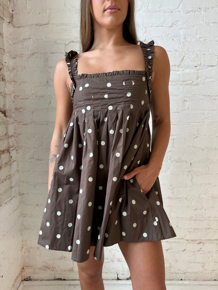 Woman wearing brown polka dot babydoll style mini dress with clear heel.