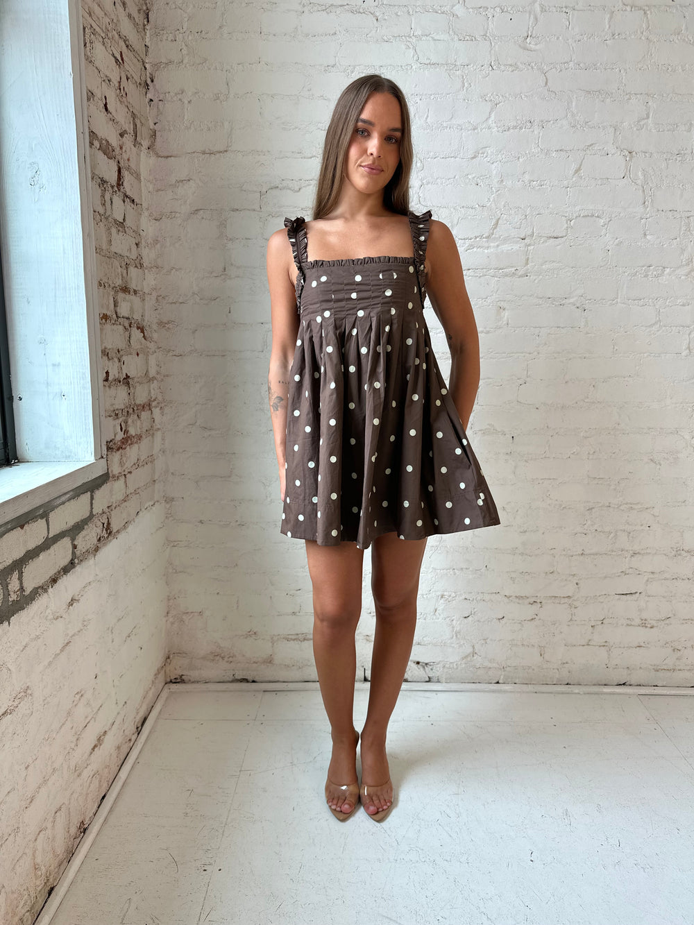 Woman wearing brown polka dot babydoll style mini dress with clear heel.