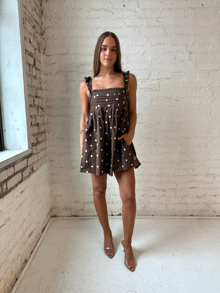 Woman wearing brown polka dot babydoll style mini dress with clear heel.