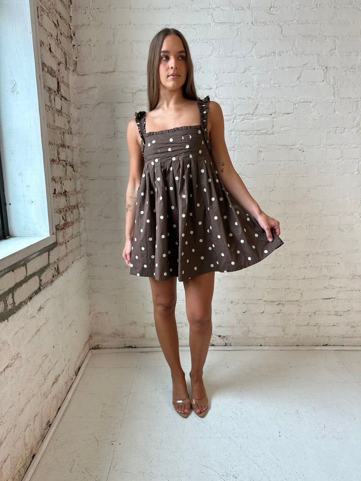 Woman wearing brown polka dot babydoll style mini dress with clear heel.