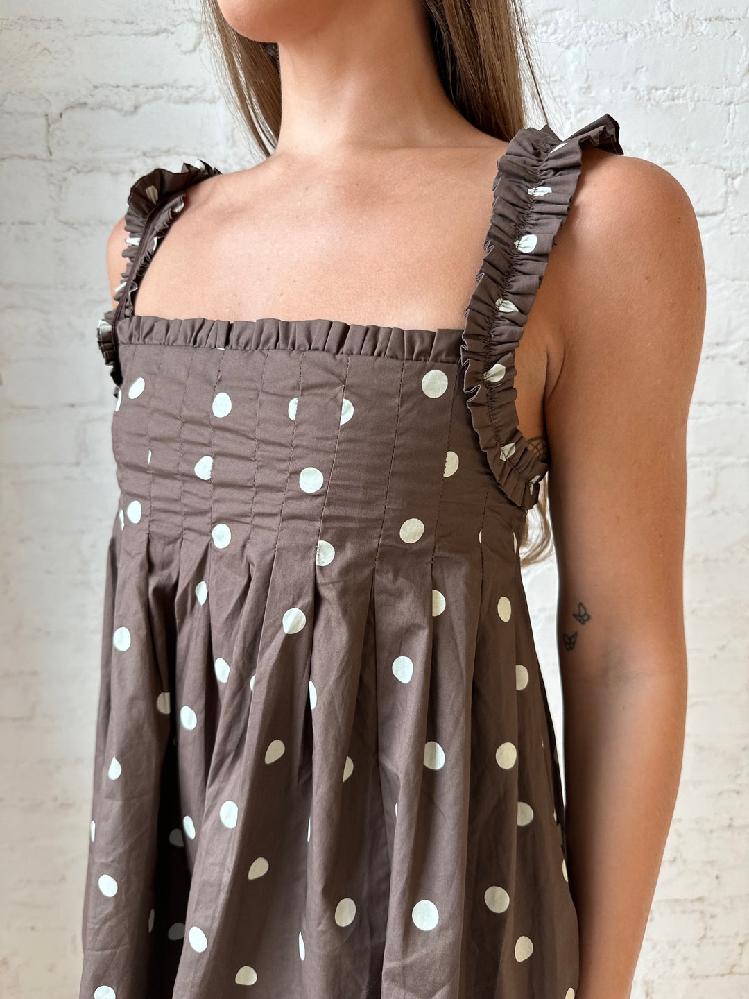 Woman wearing brown polka dot babydoll style mini dress with clear heel.
