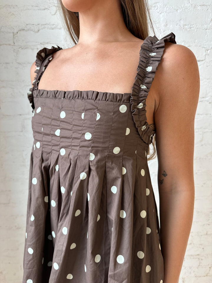 Woman wearing brown polka dot babydoll style mini dress with clear heel.