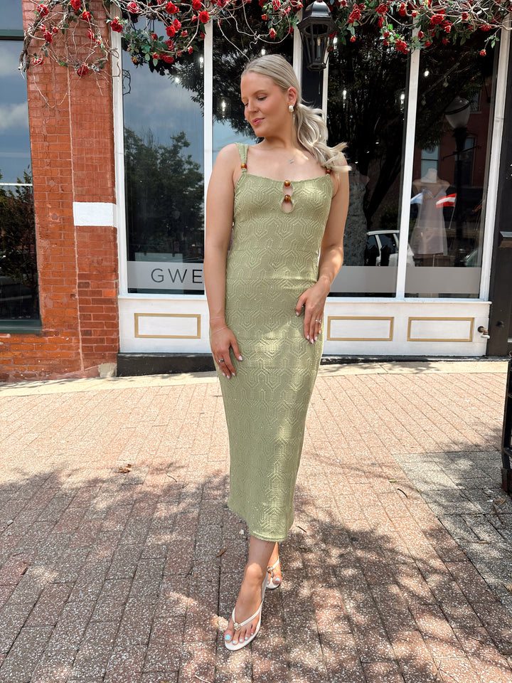 Woman wearing olive green knit maxi dress with subtle sequin shimmer and beaded detailing. 