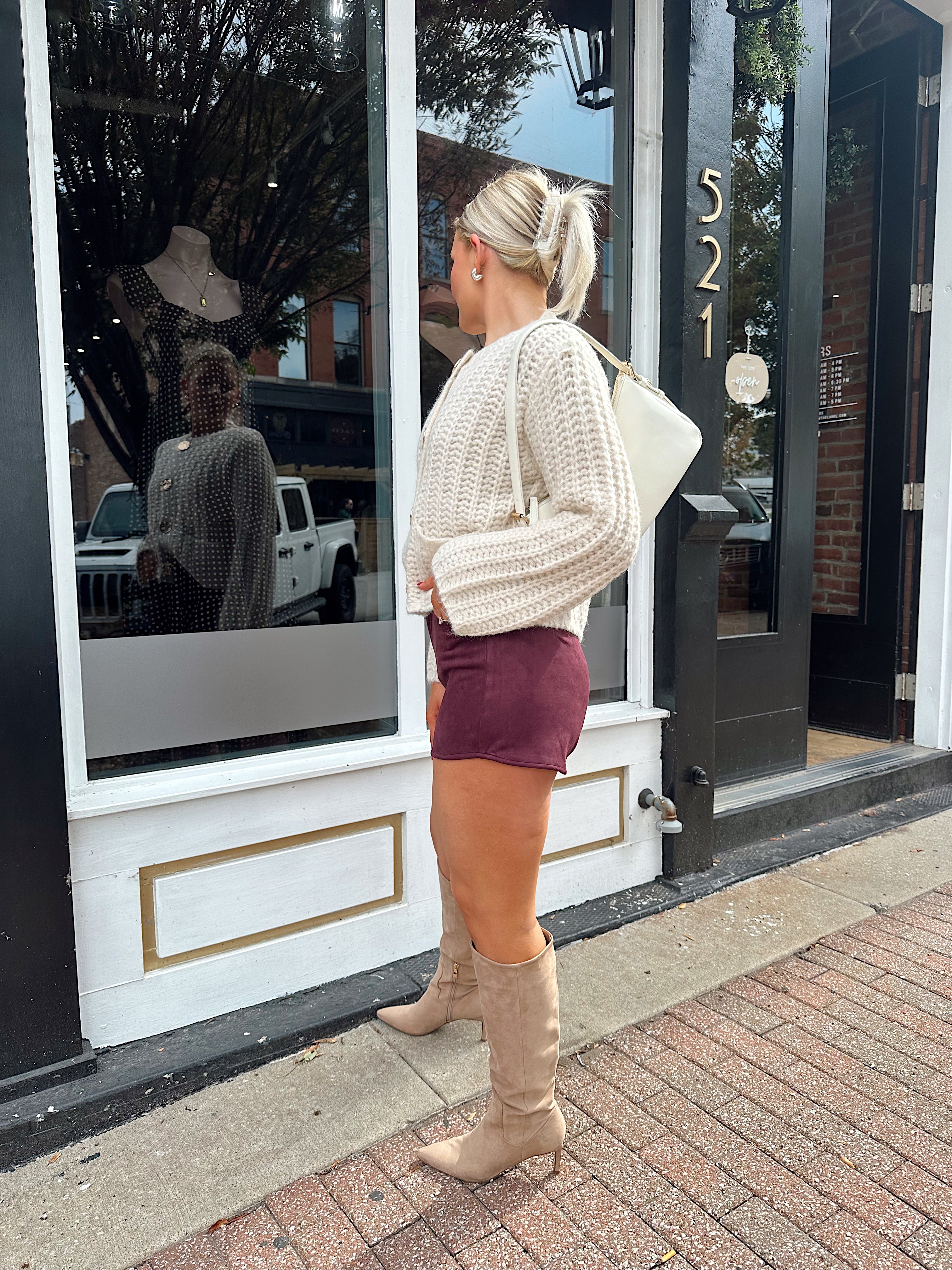 Woman wearing burgundy suede shorts with cream knit cardigan. 