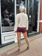 Woman wearing burgundy suede shorts with cream knit cardigan. 